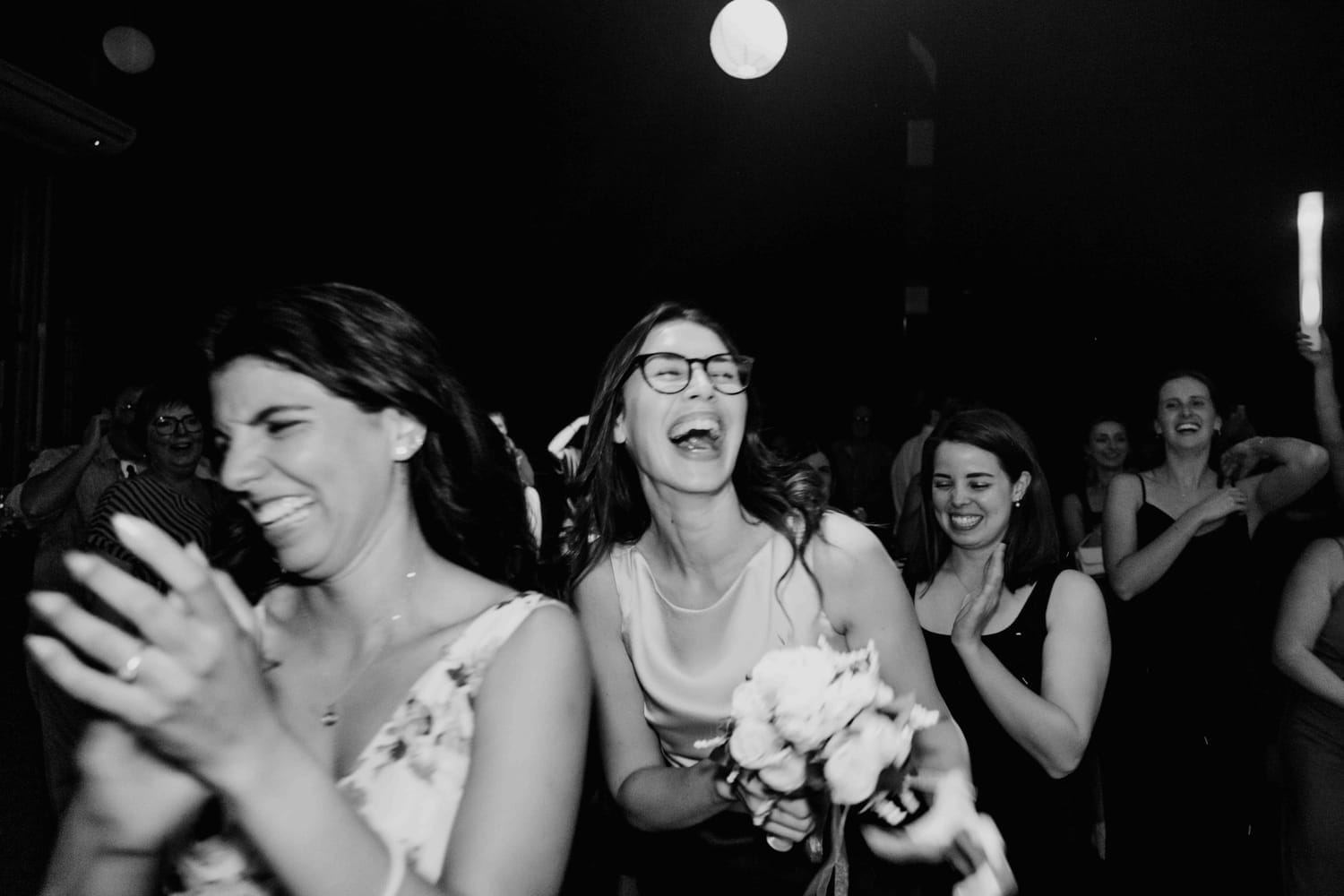 Guests laughing as one of them catches the bouquet, in black and white